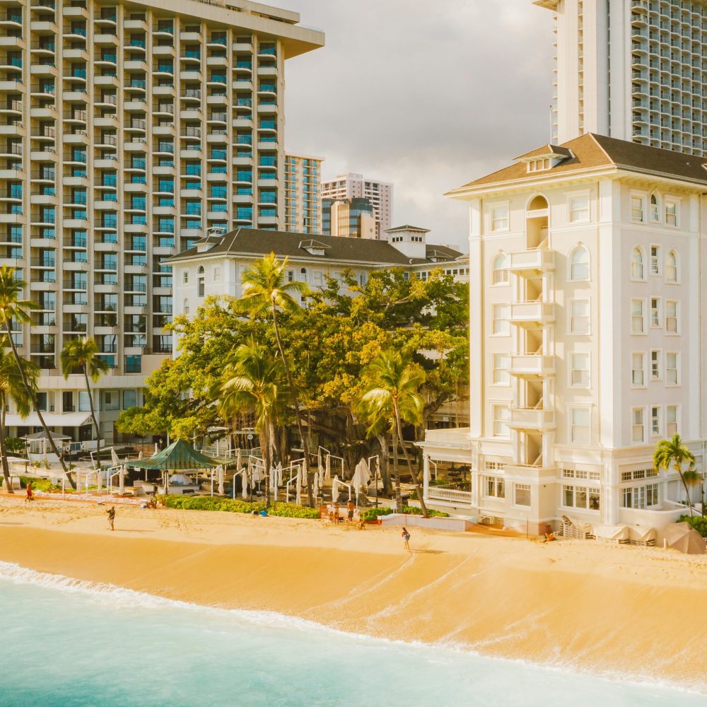 Luxury tropical beachfront hotels with palm trees and golden sand under a bright sky.